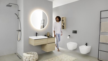 Čovjek ulazi u kupaonicu s umivaonikom, WC školjkom, bideom i kupaonskim namještajem iz serije kupaonica Geberit iCon